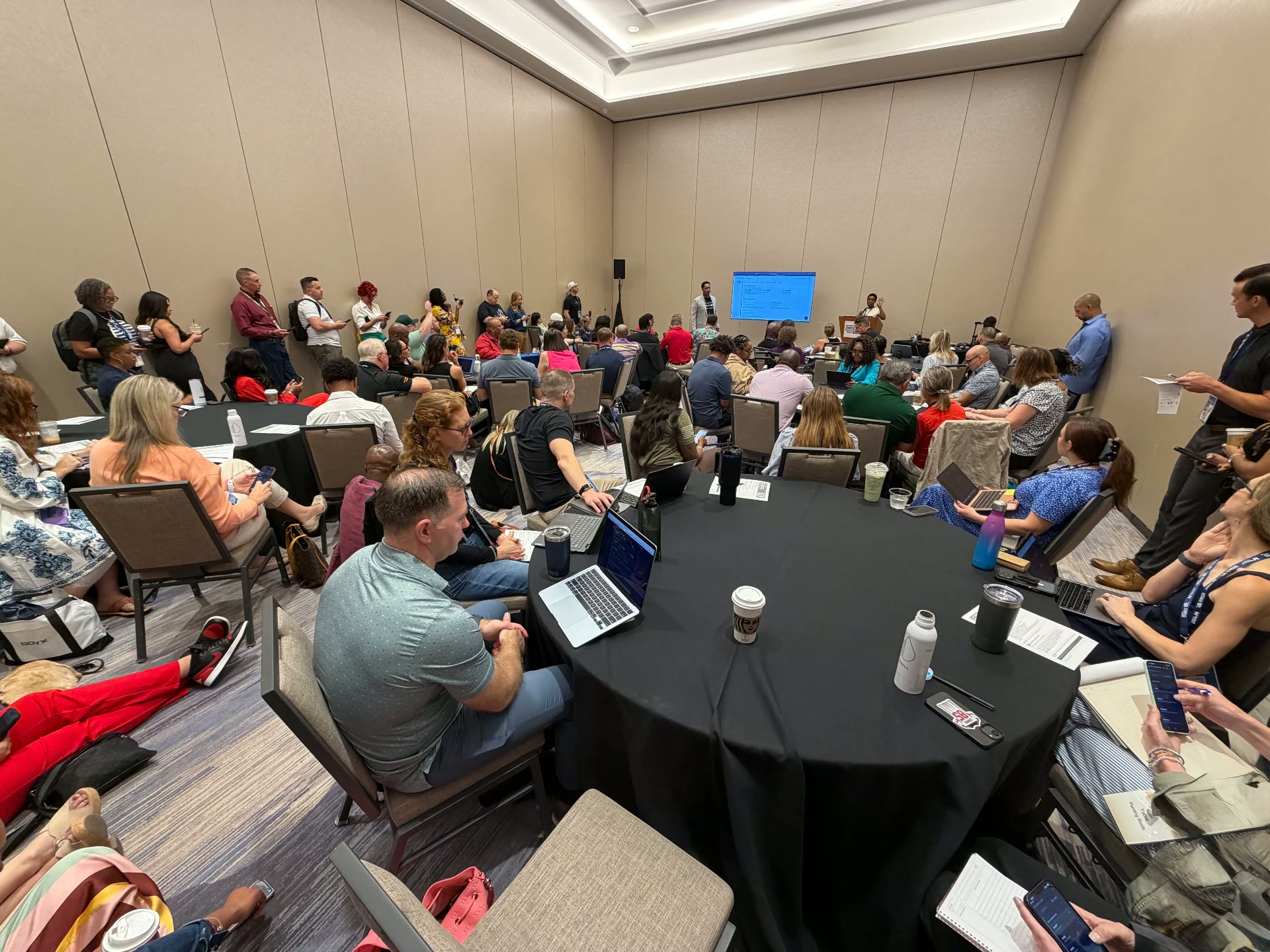 A packed AI Readiness Lab room at the Military Influencer Conference, with attendees seated at round tables and standing along the walls working on laptops